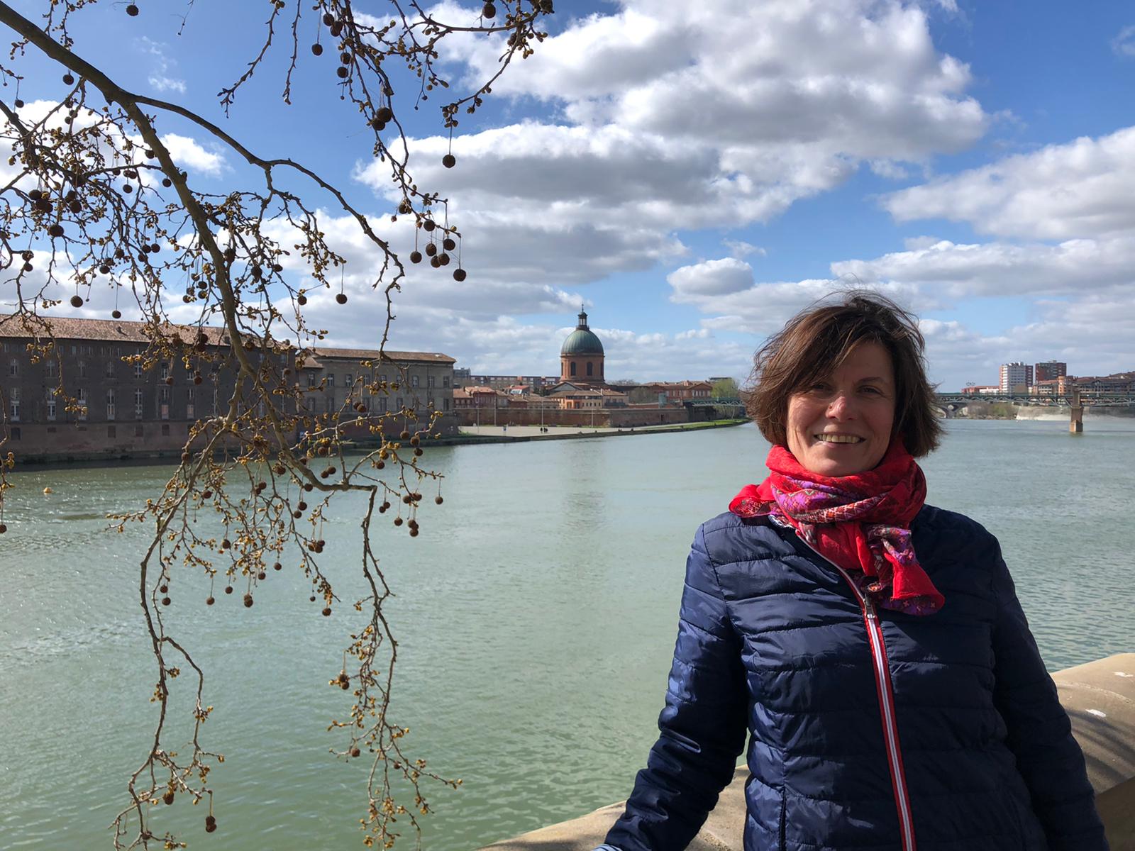 Die Heilpraktikerin Heike Gabriel lehnt an einer Brüstung vor einem Fluss, der Himmel ist bewölkt.